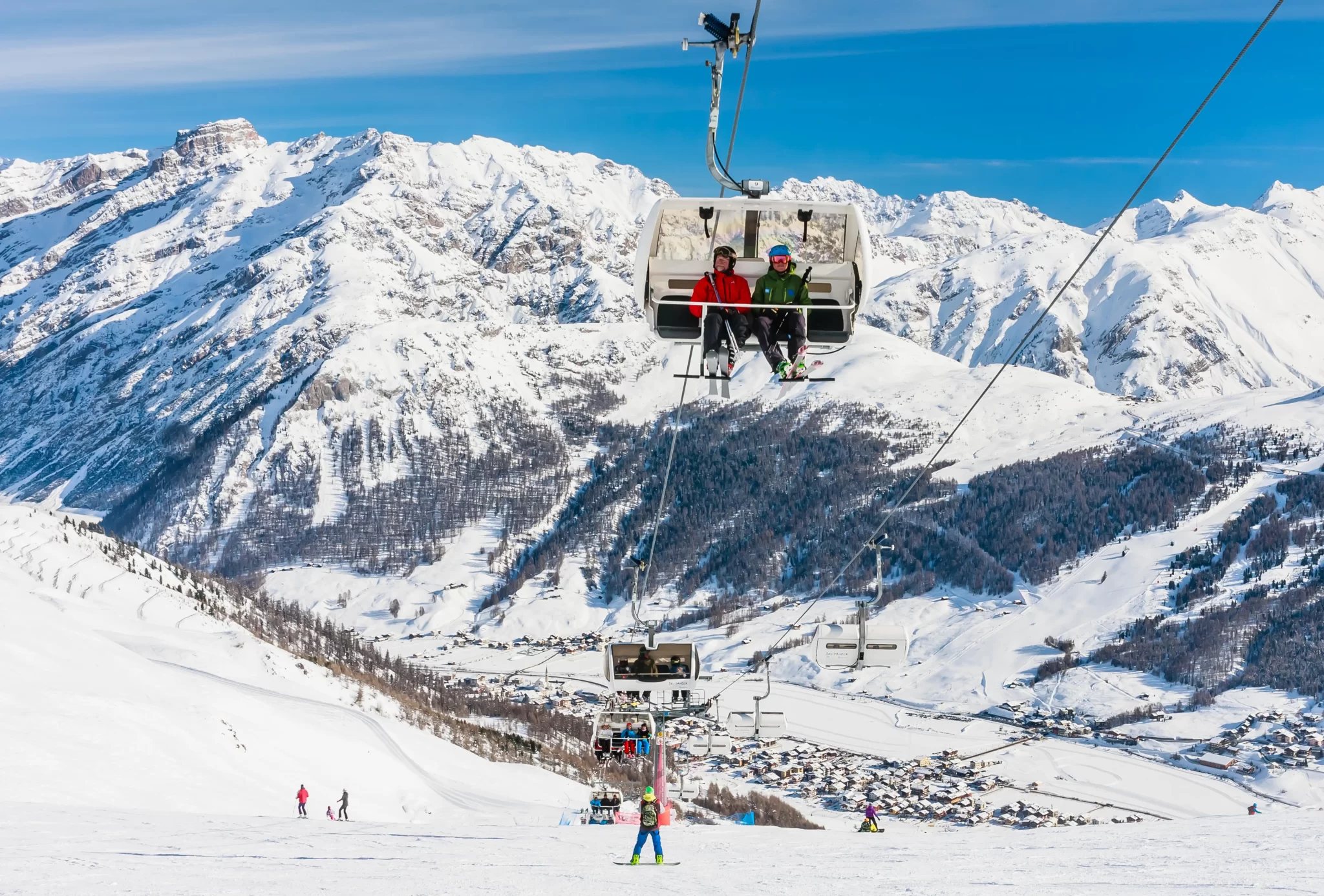 Scenico paesaggio montano innevato con seggiovia e sciatori.