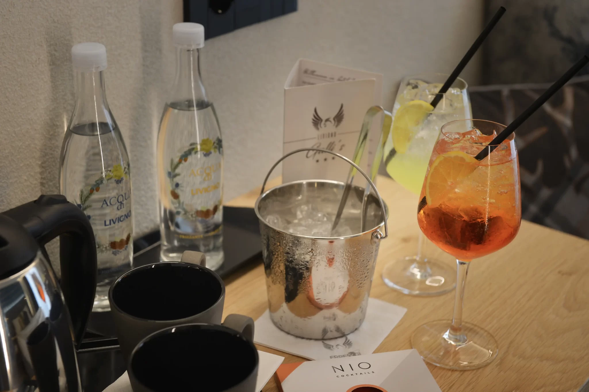 Bottiglie d'acqua minerale e cocktail su un tavolo con secchiello del ghiaccio d'acciaio.