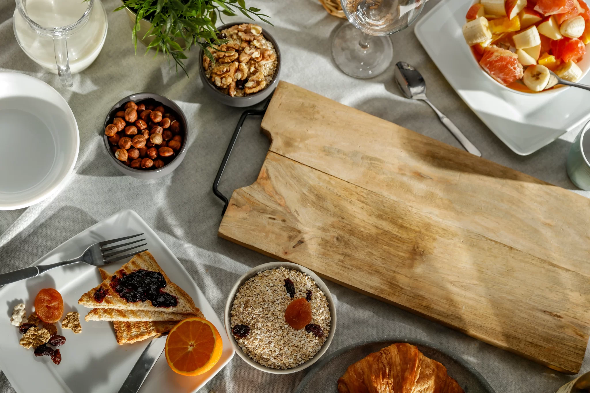 Colazione con pane tostato, marmellata, frutta fresca, noci e cereali su un tavolo.