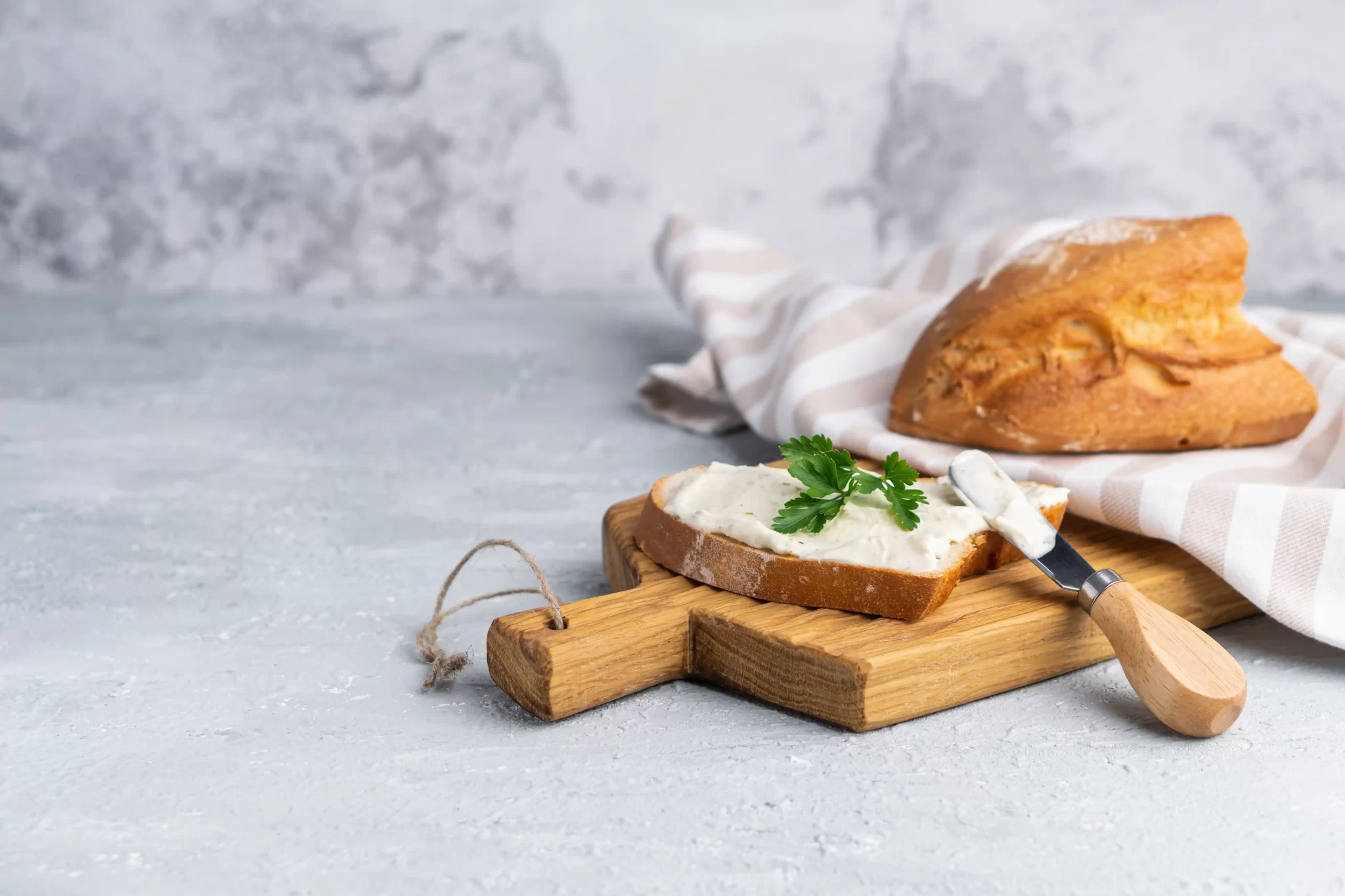 Fetta di pane con crema spalmabile e prezzemolo su un tagliere di legno.