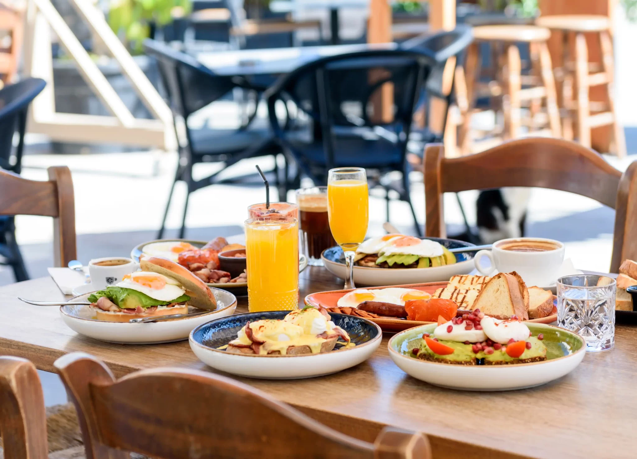 Colazione abbondante su un tavolo all'aperto con piatti assortiti e bevande.