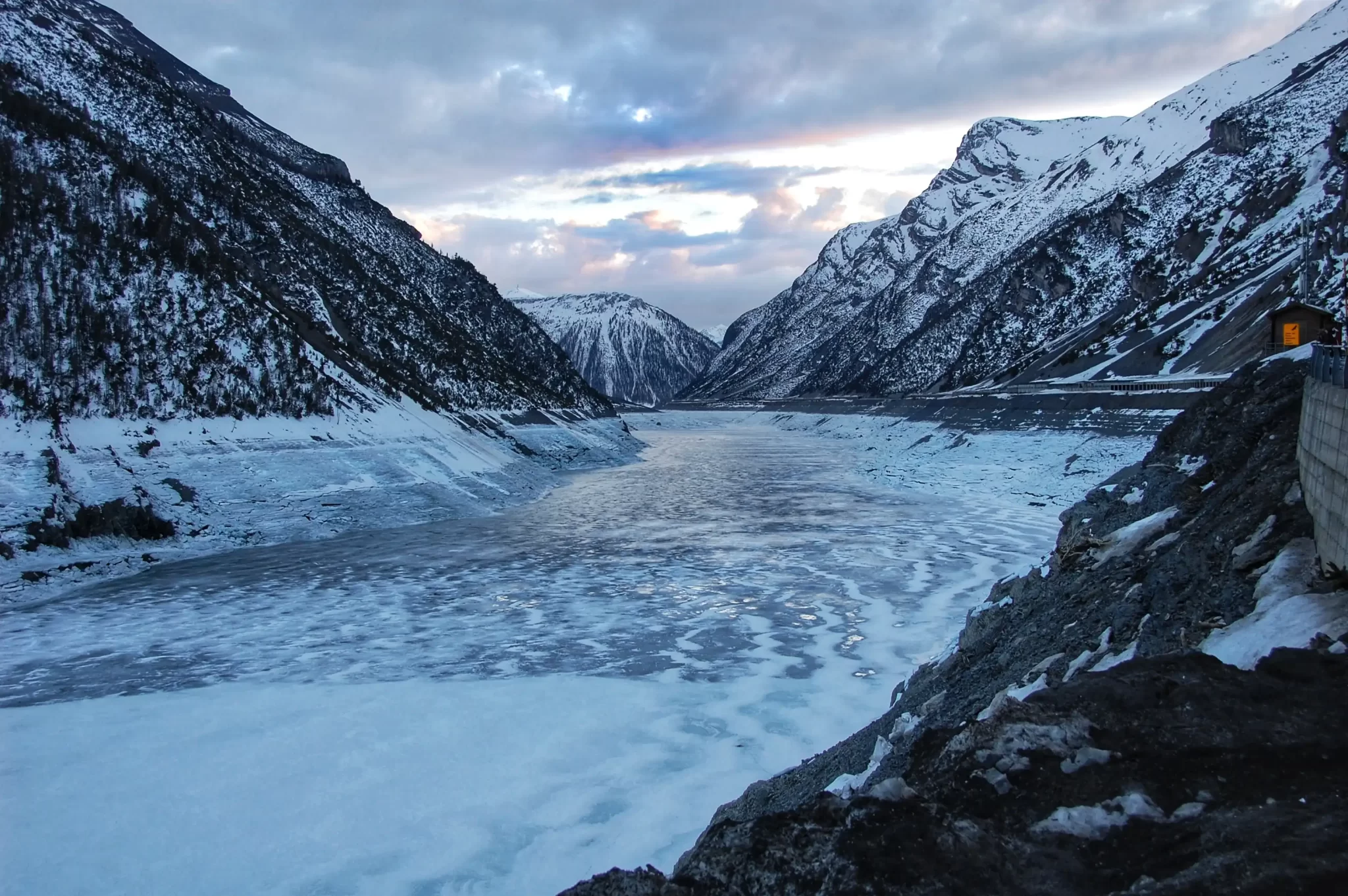 Panorama di una valle montana innevata con un fiume ghiacciato al tramonto.