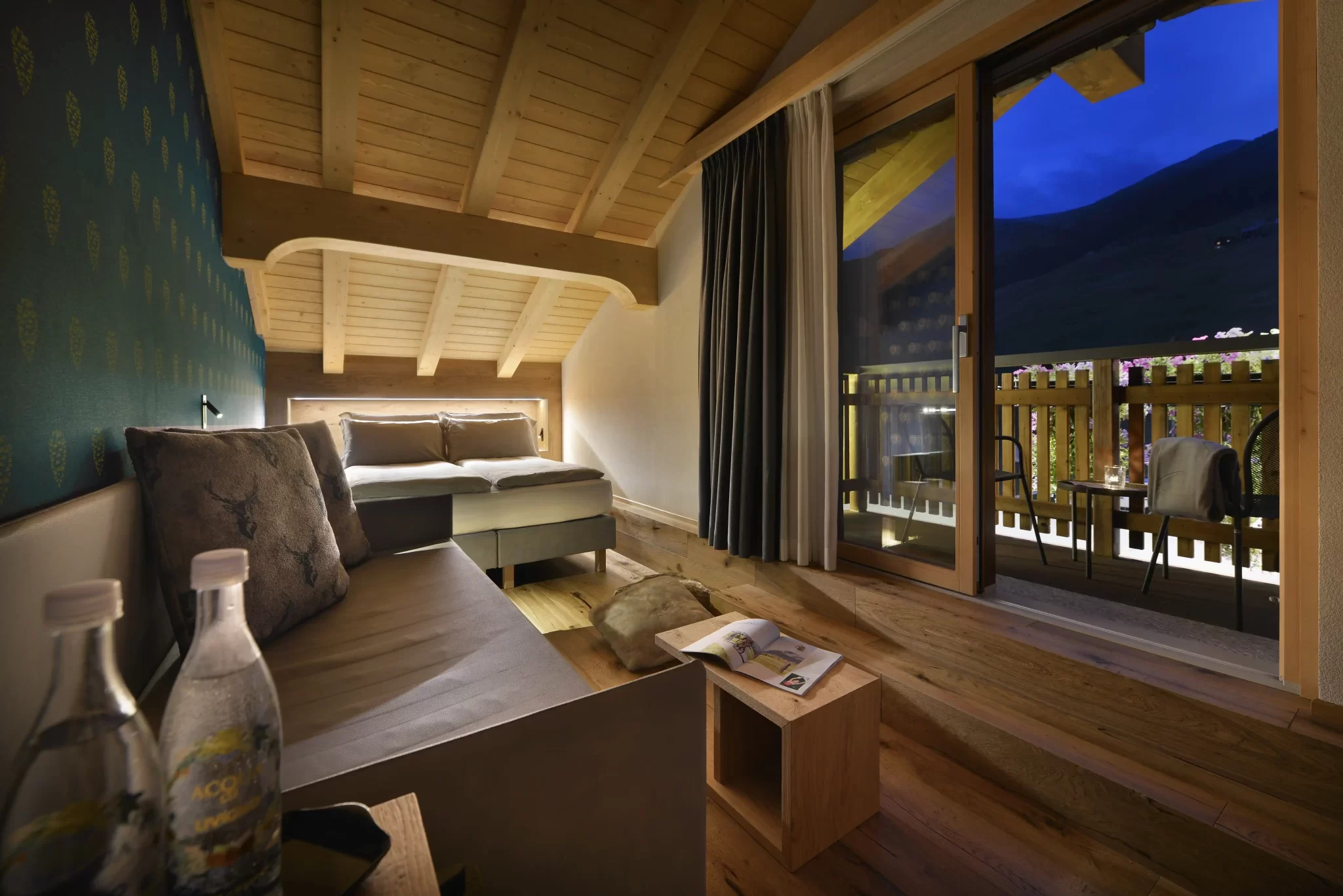 Camera accogliente con vista su una terrazza e montagna al tramonto, arredata con legno e decorazioni eleganti.