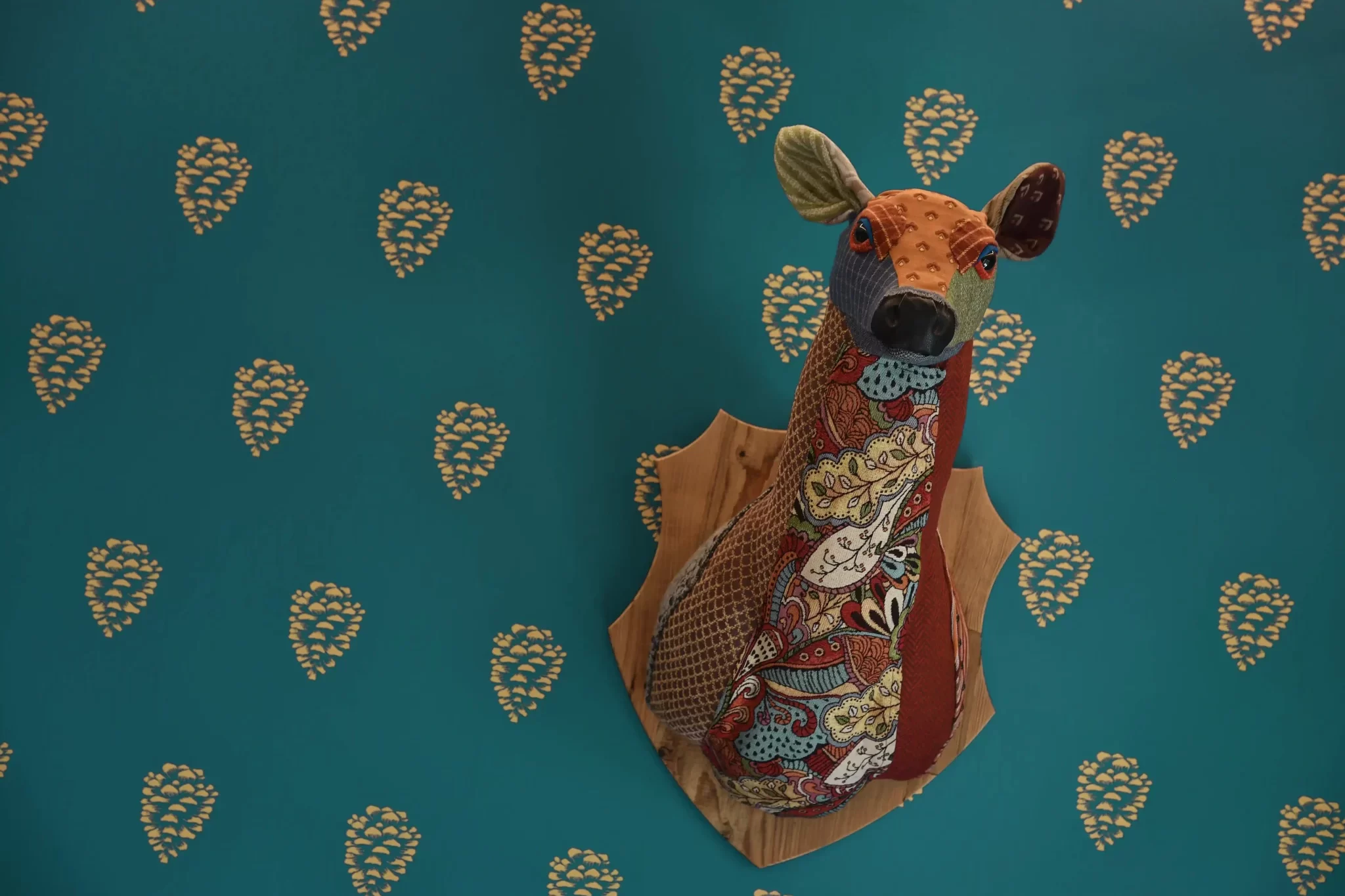 Scultura di un cervo tessile multicolore su sfondo blu con motivi di pigne dorate.