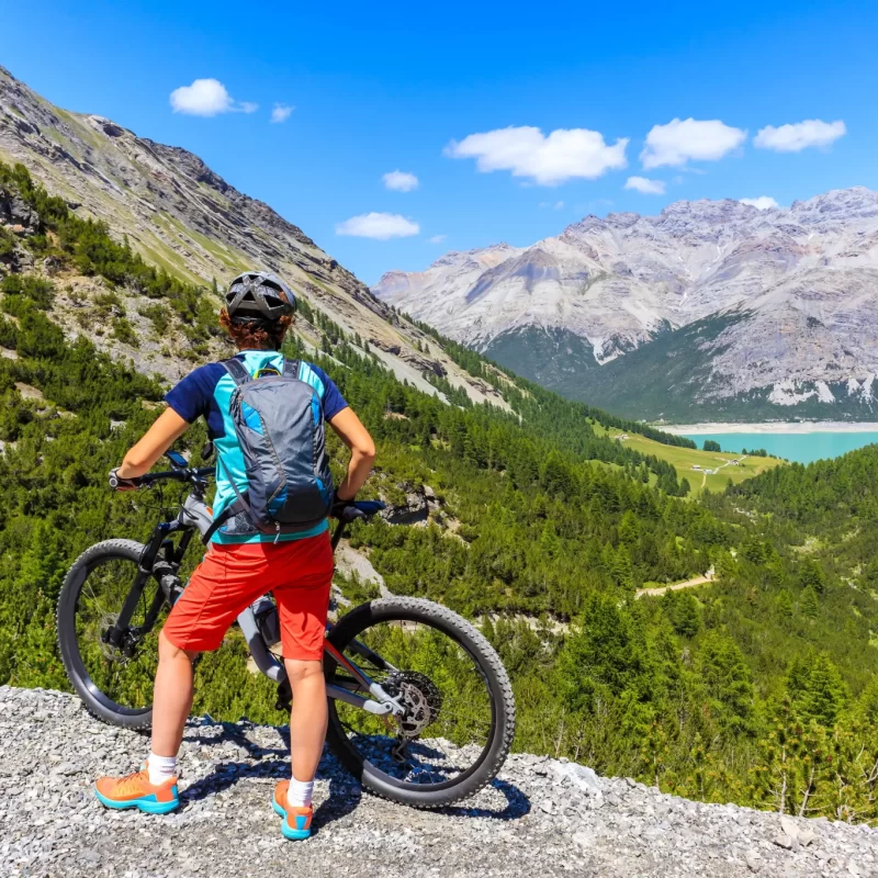 Una persona in mountain bike ammira il panorama montuoso con un lago in lontananza.