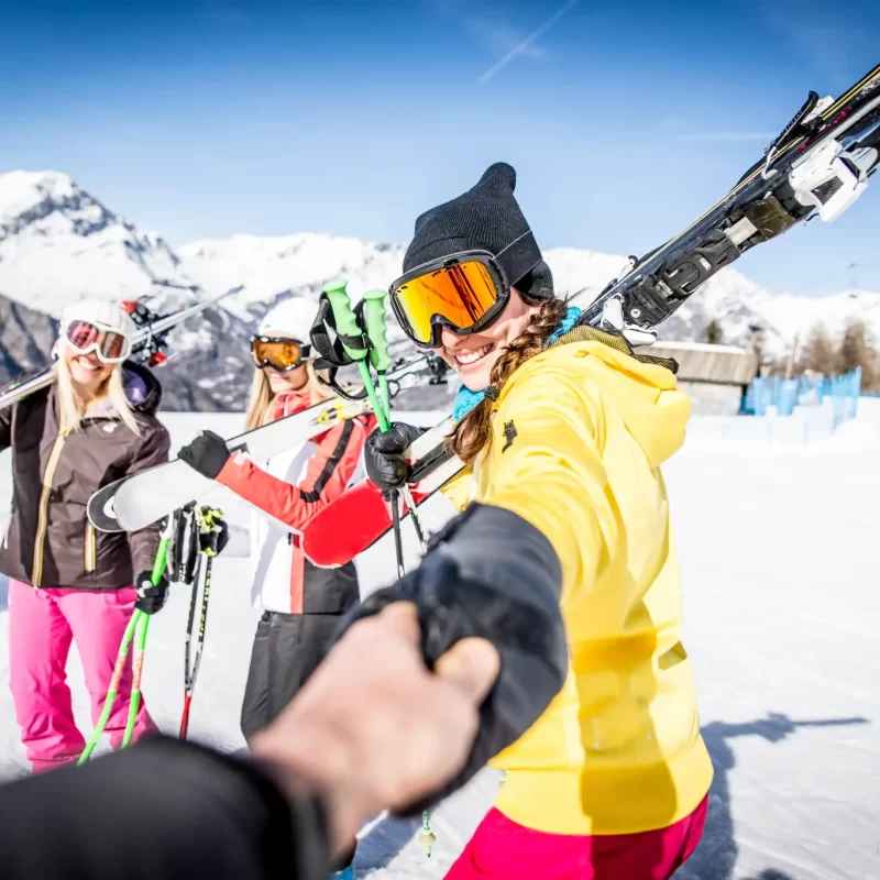 Persone sorridenti con sci in spalla sulle piste innevate di montagna.