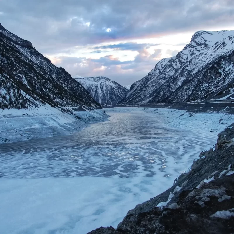 Panorama di una valle montana innevata con un fiume ghiacciato al tramonto.