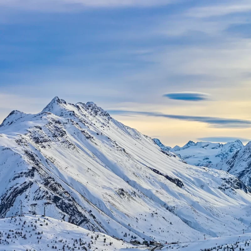 Montagne innevate sotto un cielo azzurro al tramonto.