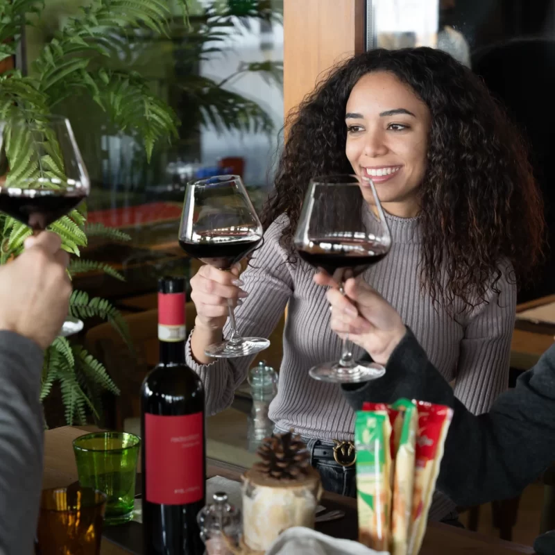 Tre persone brindano con bicchieri di vino rosso in un ambiente conviviale.