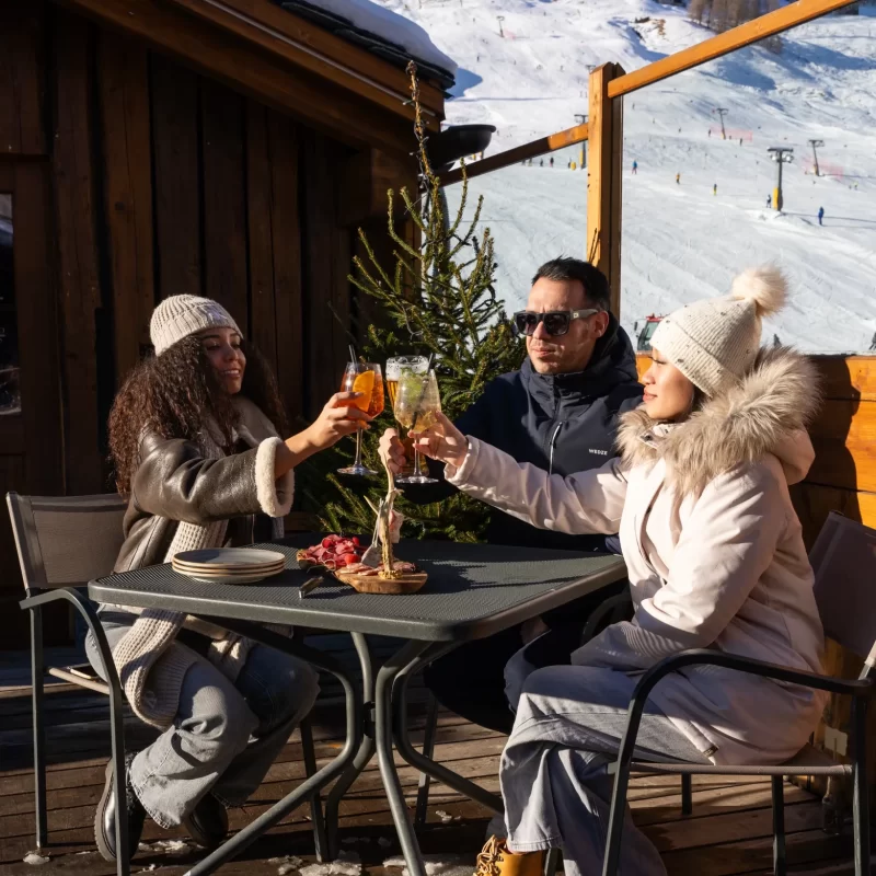 Tre persone brindano all'aperto in una località sciistica innevata.